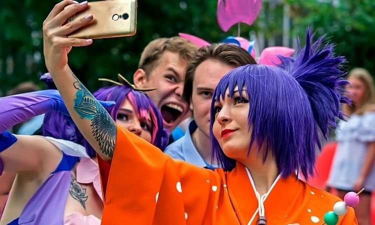 Personne en cosplay kimono orange et perruque violette se prenant en photo avec trois autres personnes dont une en cosplay