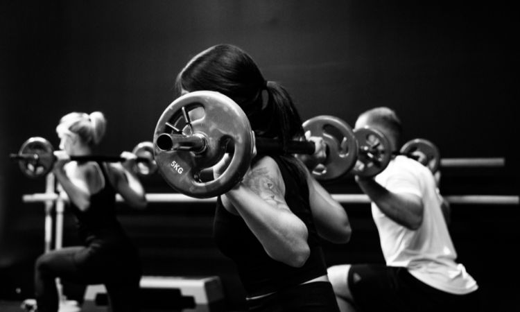 Photo en noir et blanc montrant trois personnes faisant du fitness avec des poids sur les épaules