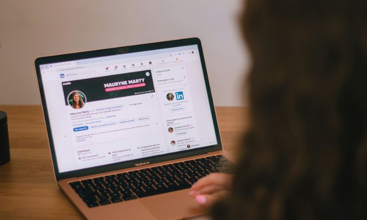 Gros plan sur l’ordinateur portable d’une personne de dos avec écran montrant un profil LinkedIn